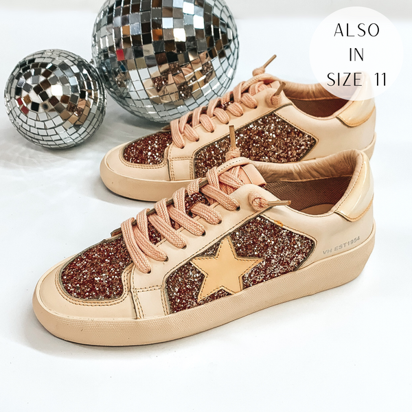 Pictured are a beige colored pair of sneakers with rose gold glitter throughout. These shoes are pictured on a white background with disco balls in the background.