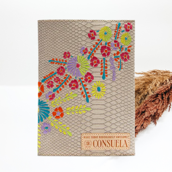 A light grey snakeskin notebook with a colorful, flower embroidery across the notebook. This notebook is pictured on a white background with tan and brown pompous grass behind the notebook.