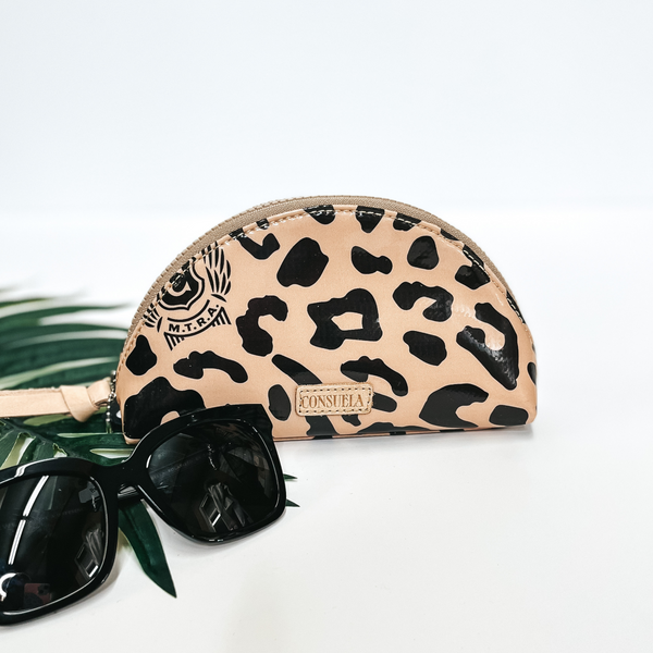 A leopard print dome shaped cosmetic case pictured on white background with black sunglasses and a palm leaf.