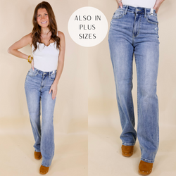 Model is wearing a pair of light wash jeans in a straight leg style. Model has these jeans paired with tan clogs, a white bodysuit, and gold jewelry.