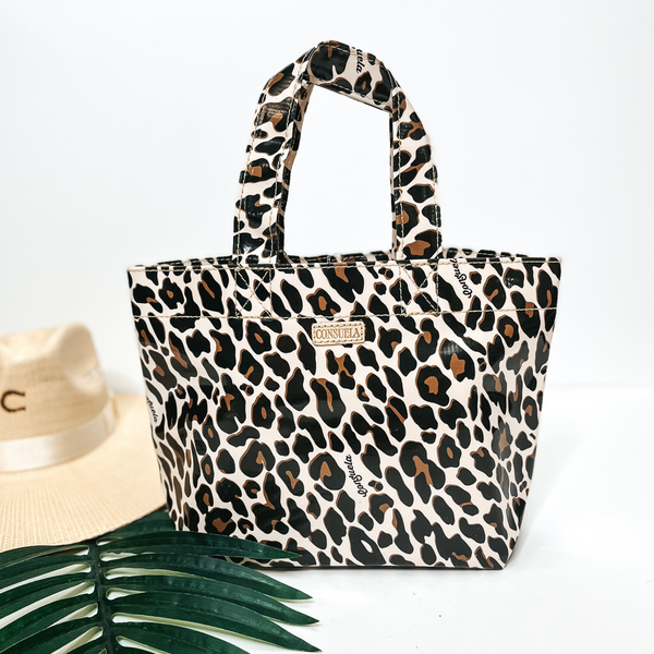 A small size leopard print bag with handles. Pictured on white background with palm leaf and straw hat.