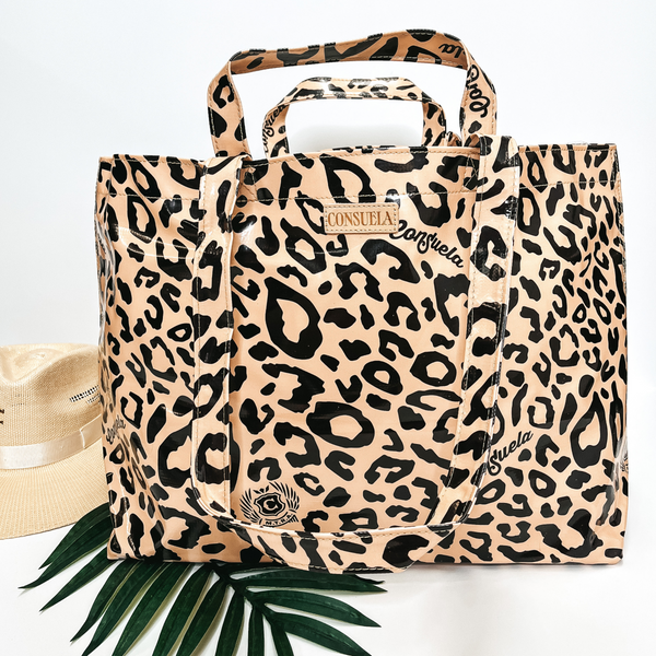 A large size leopard print bag with handles. Pictured on white background with palm leaf and straw hat.