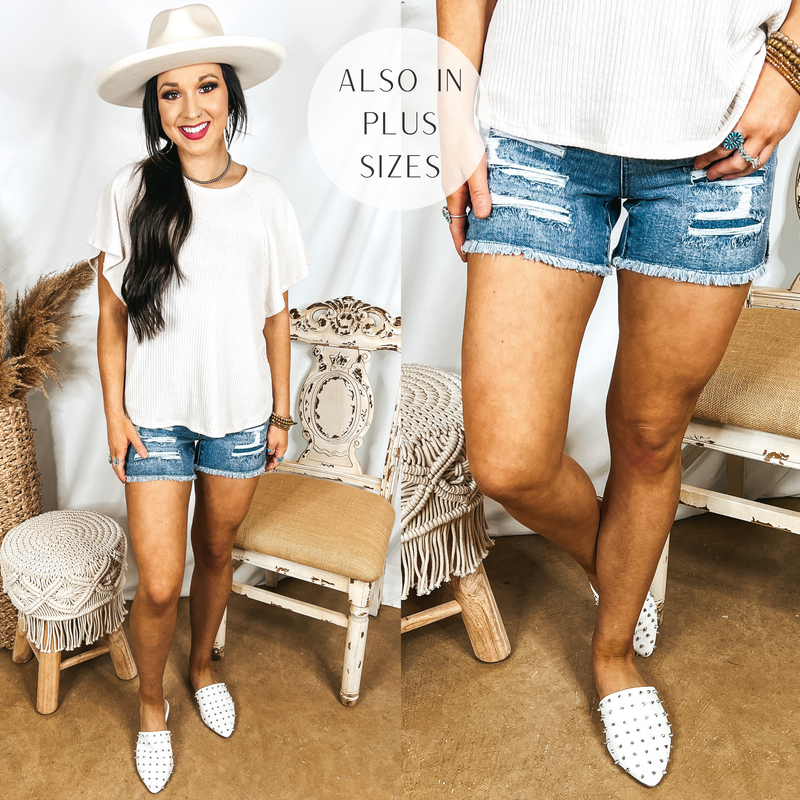 Model is wearing a pair of patch denim shorts with a raw hem. Model has it paired with white mules, a white top, and an ivory hat.