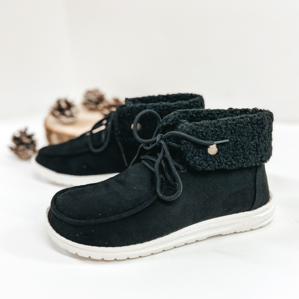 Black shoes with a black fleece lining and white sole. Pictured on white background with pinecones.