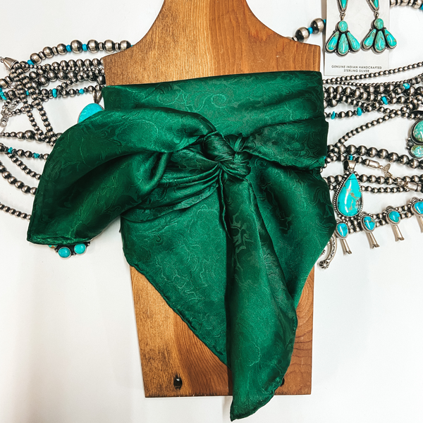 A jacquard print wild rag tied around a wooden display. Pictured on white background with sterling silver and turquoise jewelry.