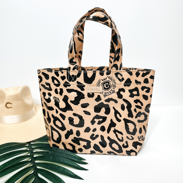 A small size leopard print bag with handles. Pictured on white background with palm leaf and straw hat.