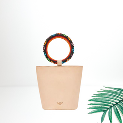 A leather bucket bag with circle beaded bangle handles. Pictured on a white background with a palm leaf.
