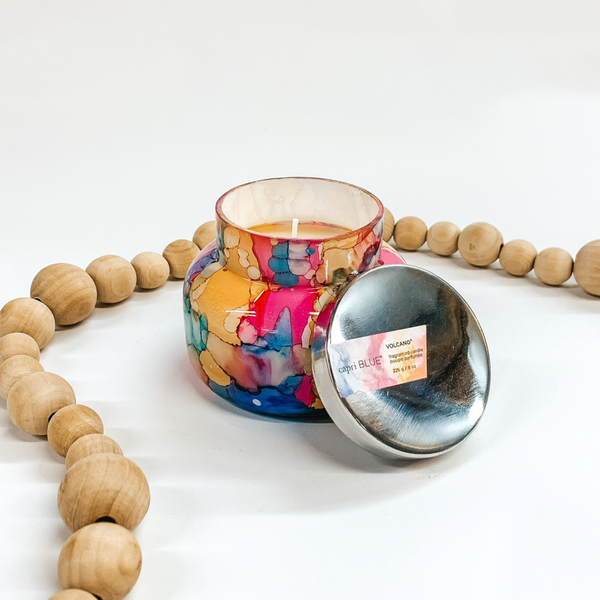 A rainbow watercolor jar candle with a metal lid. Pictured on white background with wooden beads.