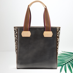 A black leather bag with leopard print sides. Pictured on white background with a palm leaf.