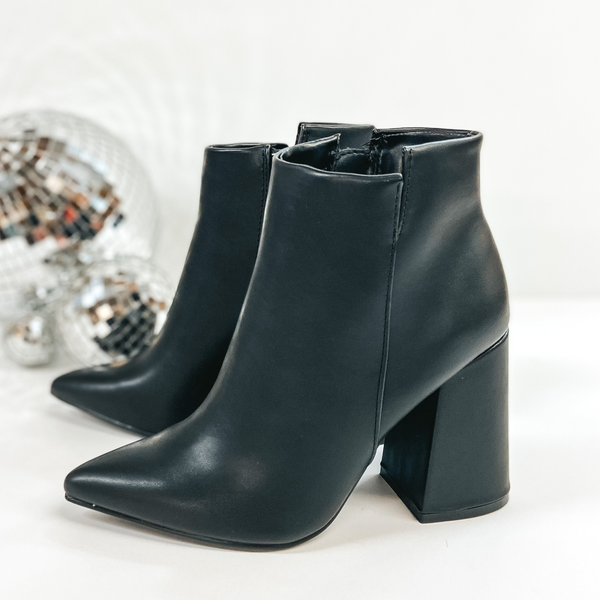 These booties have a high block heel with an asymmetrical ankle. The zip up booties have a pointed toe and are pictured on a white background with disco balls.