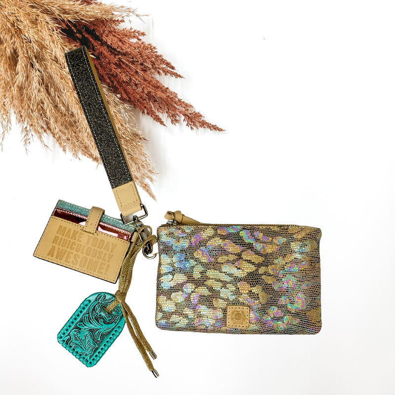 In the middle of the picture is a wristlet that has a card holder and tooled keychain attached, in an iridescent leopard print. background is solid white with florals laid on the top left.  