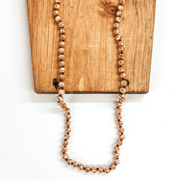 Latte crystal beaded necklace. This necklace is pictured on a brown block on a white background.