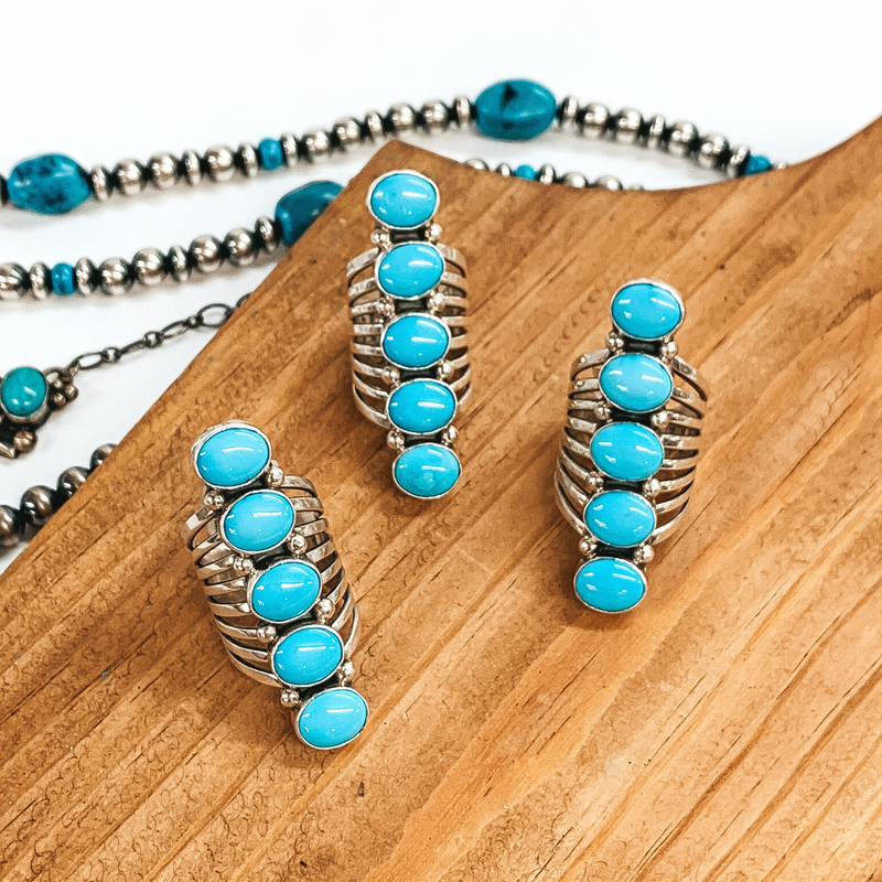 Sterling silver rings with five turquoise stones. These rings are pictured on a brown block on a white background