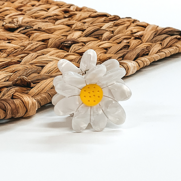 Flower shaped clip in white with a yellow center. This clip is pictured on a white background with a basket weave behind the clip.