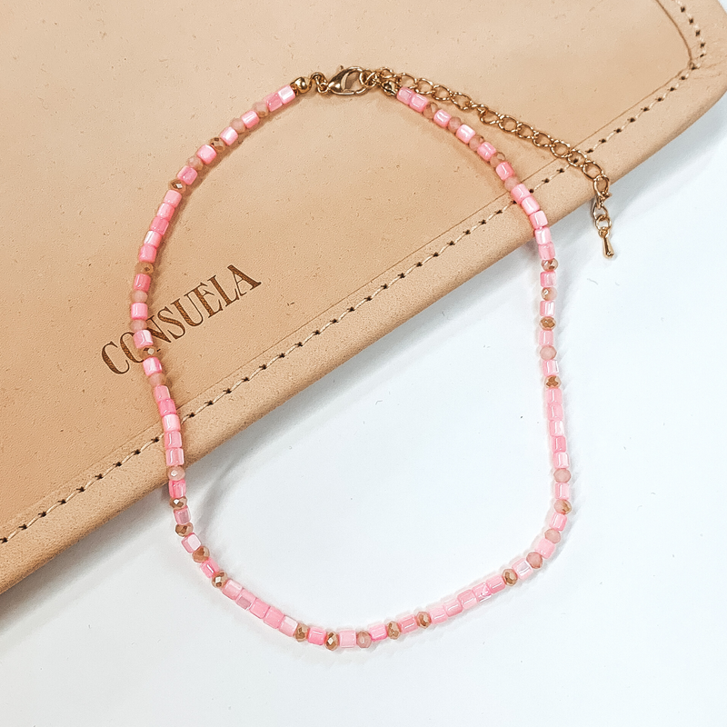 Pink beaded necklace that is pictured on a white and tan background.