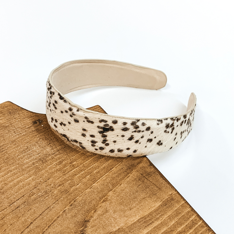 Ivory headband with dark brown spots and an ivory underside. This headband is pictured laying partially on some dark wood on a white background.