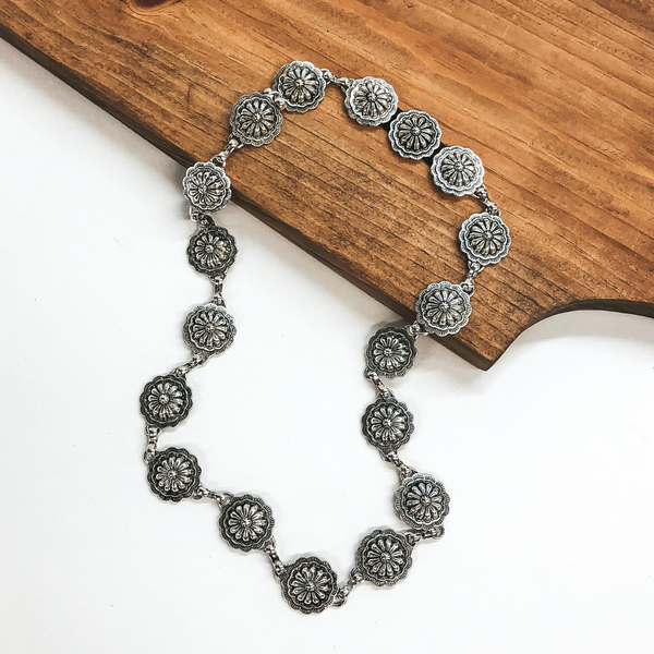 Silver, circle concho hat band. This hat band is pictured partially laying on a brown block on a white background.