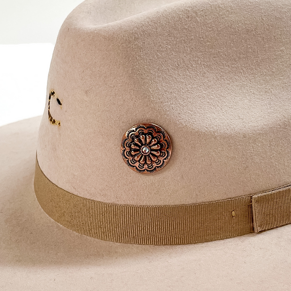 Copper, circle concho with detailed engraving and a small, center AB crystal hat pin. This hat pin is pictured on a beige hat and white background. 