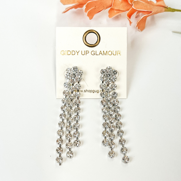 Clear crystal tassel earrings with a silver backing. These earrings are pictured on a white background with an orange flower above the earrings.