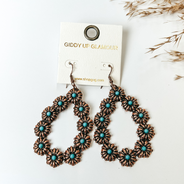 Copper flower concho outline teardrop earrings with center turquoises stones in each concho. These earrings are pictured on a white background. 