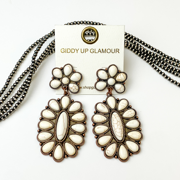 Copper, oval drop earrings with ivory stones. These earrings are pictured on a white background with silver beads behind the earrings. 