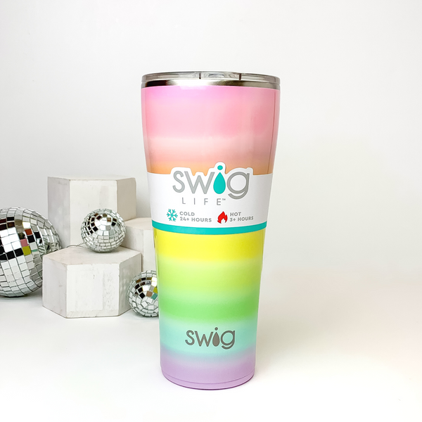 Ombre rainbow tumbler with a clear lid. This tumbler is pictured on a white background with white blocks and disco balls on the left side of the picture. 