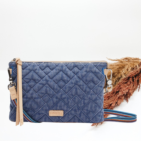 Pictured is a rectangle crossbody purse. This is a blue denim print with stitched design. This purse is pictured on a white background with pompous grass on the right side of the picture.
