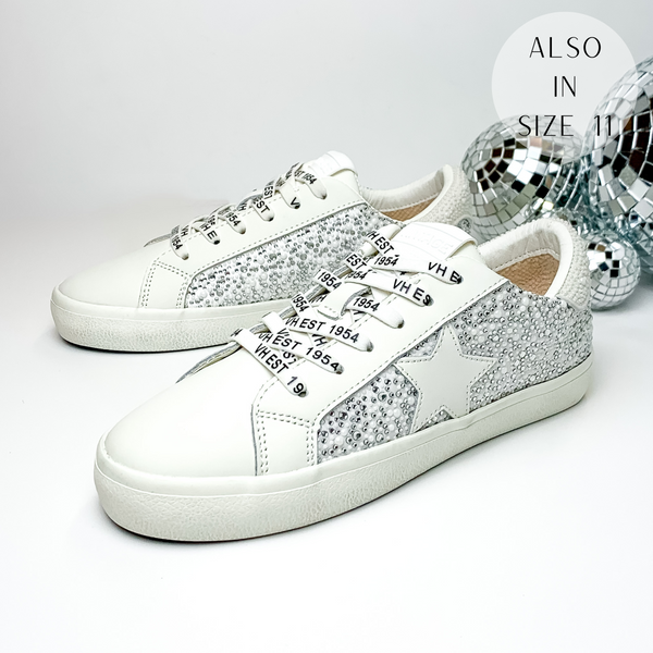 White tennis shoes with a white pearl and clear crystal design over the side of the shoe and the heel. These shoes also have a white star emblem on the side of the shoe. These shoes are pictured on a white background with disco balls behind them on the right hand side.