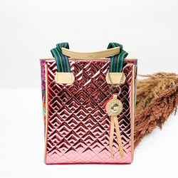 Metallic pink color tote with a stitched pattern. This tote has striped handles with tan handles, multicolor sides, and a tan leather charm. This tote is pictured in front of pompous grass on a white background.