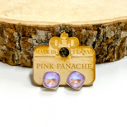 A pair of silver, square stud earrings with lavender cushion cut crystals. These earring are pictured on a wood holder on a white background with a piece of wood in the background.