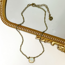 Bronze chain necklace with a water opal cushion cut crystal. This necklace is pictured partially laying on a gold mirror on a white background.