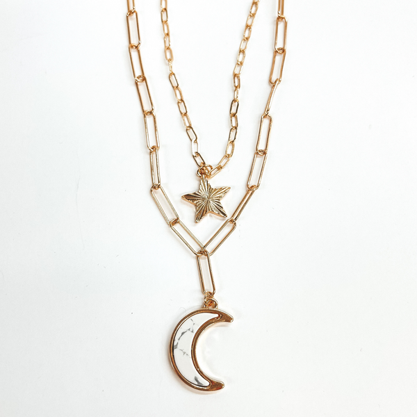 Double layered paperclip chain necklace in gold.  The shorter strand has a gold sunburst star and  the longer strand has a white stone pendant in a moon shape. This necklace is taken on a white background.