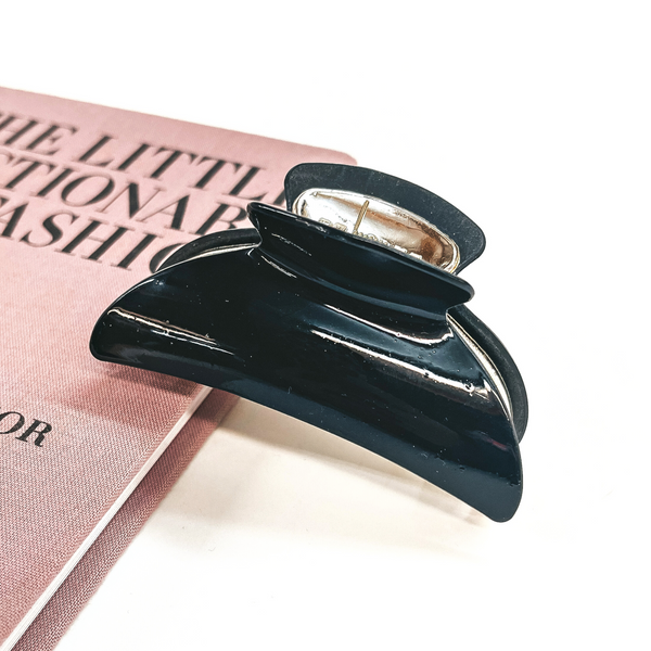 This is a black and gold tone clip leaning on a pink book and white background.