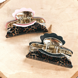 There are two dark leopard print hair clips with a gold tone inlay in light pink  and black. Both of these clips are taken on a slab of wood.