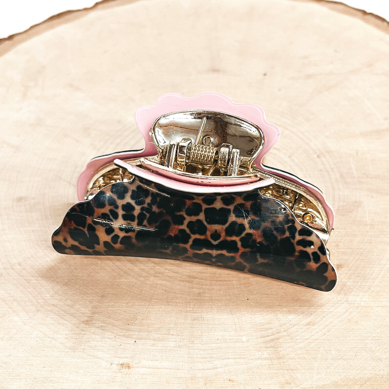 This is a dark leopard print hair clips with a gold tone inlay in light pink.  This hair clip is taken on a slab of wood and on a white background.