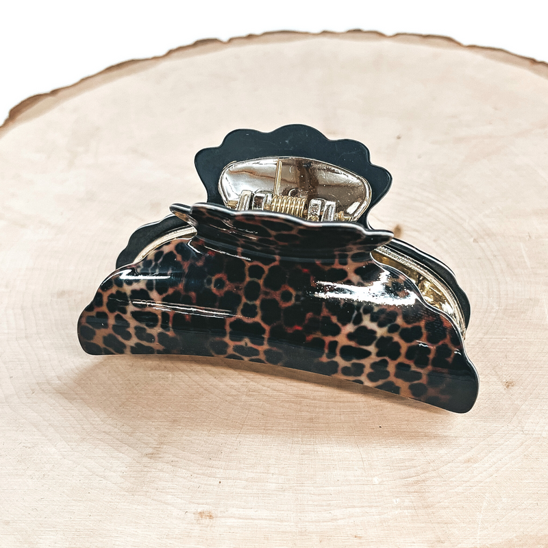 This is a dark leopard print hair clips with a gold tone inlay in black.  This hair clip is taken on a slab of wood and on a white background.