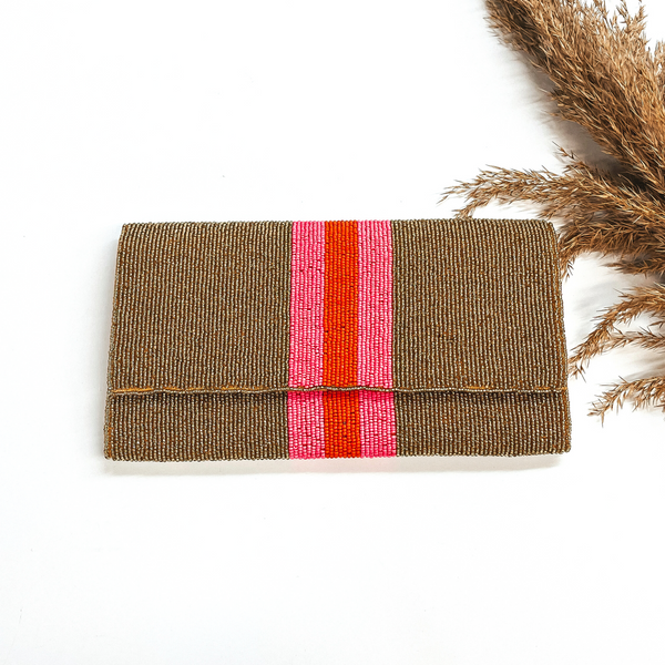 This is a seedbeaded clutch purse in  gold with  three stripes in the middle, two hot pink and one orange line in the middle. This bag  is taken laying on a white background with a brown plant in the side as decor.