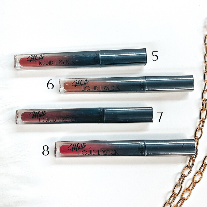 There are four liquid lipsticks in different shades of dark-nudes/red laying on a white  background with white fur and a gold link chain in the side as decor.