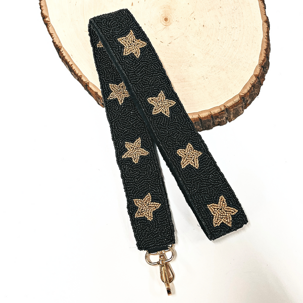 This is a black beaded purse strap with gold beaded stars all along with a gold clasp. This purse strap is taken on a slab of wood and on a white background.