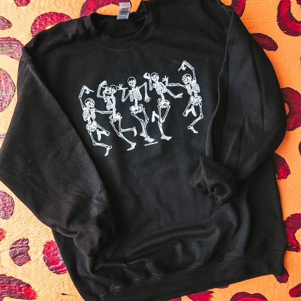 A black long sleeve graphic sweatshirt with 5 dancing skeletons. There is a pink and yellow background for this picture.