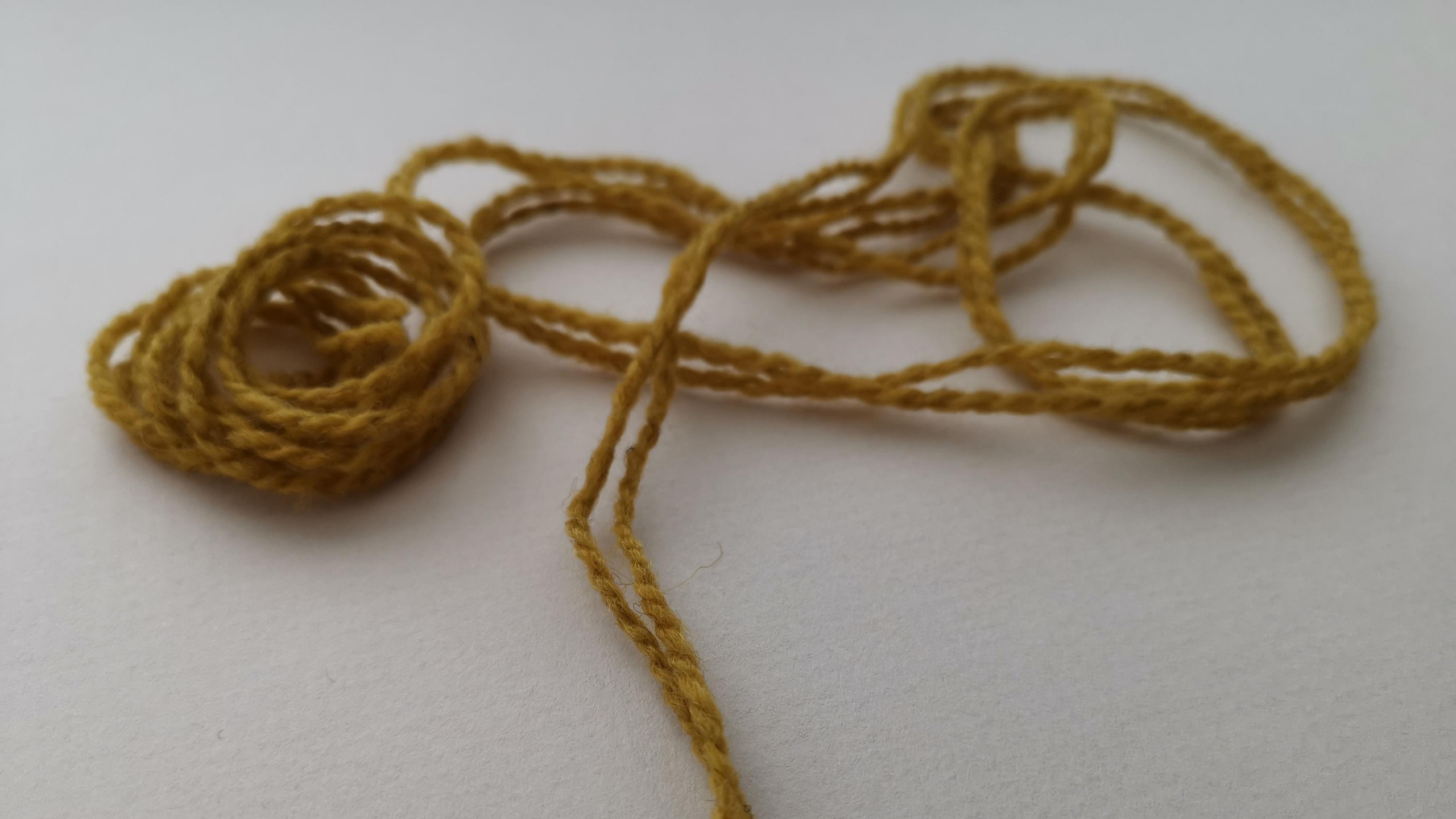 A yarn tangle of Blacker Yarns Cove in a mustard colour showing some fly away fibres and a medium twist.