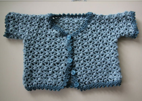 Crcoheted baby cardigan in a chunky lace pattern.  The main body is mid blue and teh trim is a picot edge in teal.  Five little blue buttons finish it off.