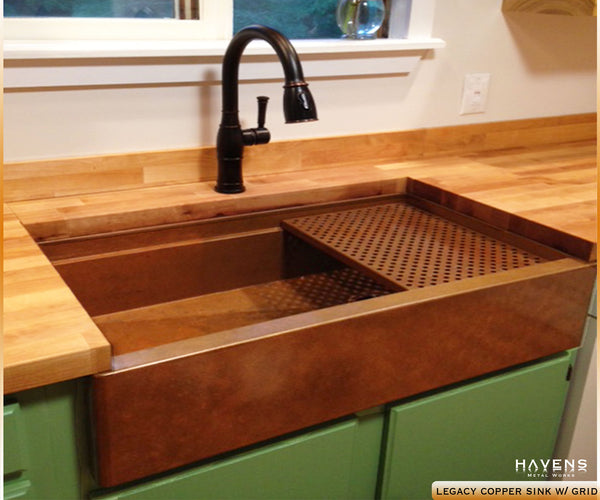 Legacy copper farmhouse sink in a kitchen with light wood countertops.