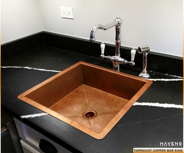 Top mount copper bar sink with faucets on a stone black countertop. 