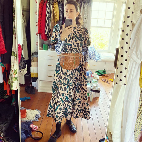 Clare Vivier Taking A Selfie In Front of A Mirror, Wearing A Cream and Blue Printed Dress with A White and Blue Striped Longsleeve Tee Underneath and Our Natural Woven Grande Fanny Around Her Waist