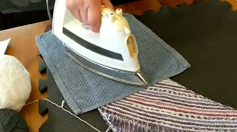 Photo of an iron over a washcloth that's placed on a knit shawl. To demonstrate how to safely steam block acrylic yarn.