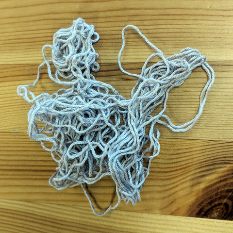 Photo of a few yards of lilac colored yarn on a wood table to illustrate the yarn leftover from this knit lace shawl project.