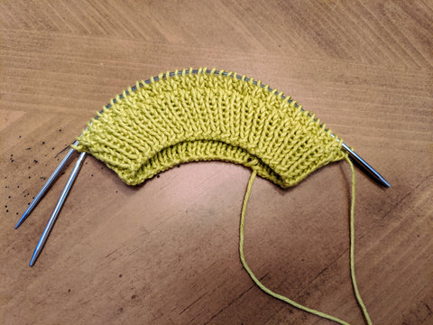 Photo of the beginning of a yellow knit hat on two circular knitting needles.