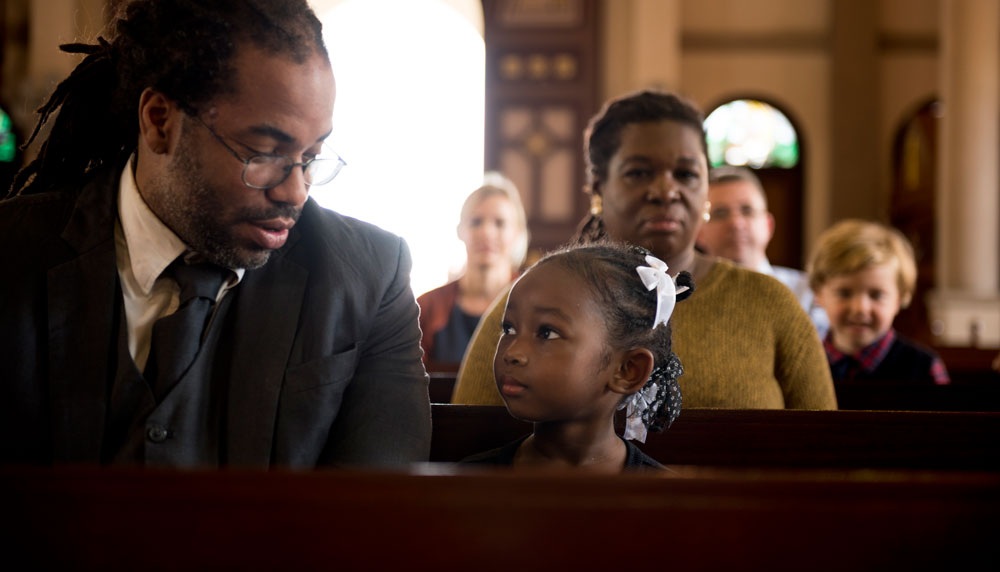 Image of church in session depicting a father with his daughter in the pews of the church.