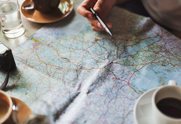 Jack Dusty CLothing and Lifestyle blog - Mans hand planning a roadtrip on a map with a coffee.